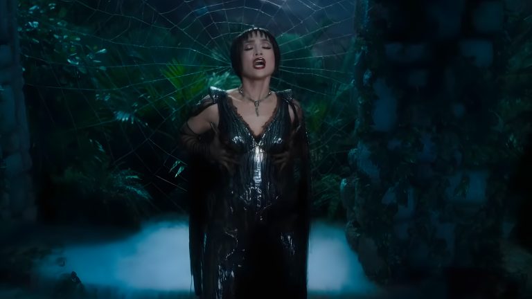 Jennifer Lopez in Kiss of the Spider Woman trailer (2025), singing in a dark fantasy sequence surrounded by a spider web.