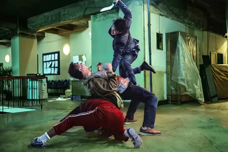 A brutal fight scene from The Furious, showing a man in a suit raising a knife over two attackers during an intense warehouse brawl.