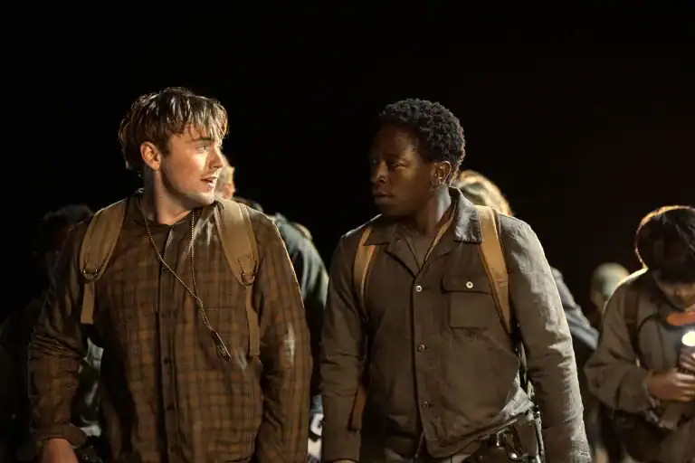 Two young men walk side by side at night with backpacks, looking tense during a grueling march in The Long Walk.