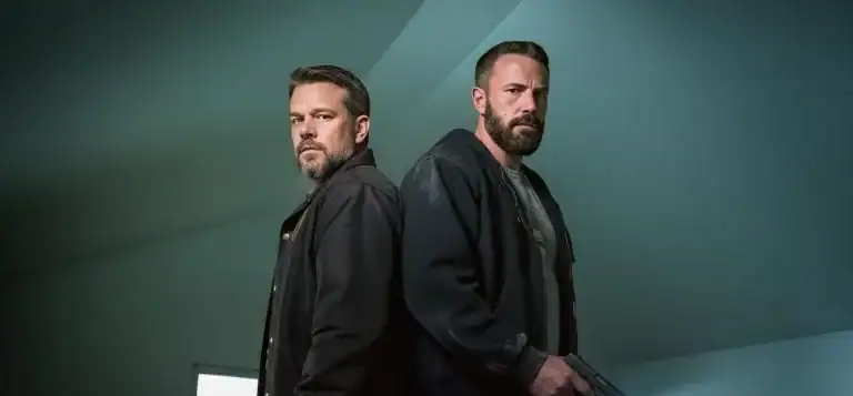 Back-to-back detectives in a teal, low-ceilinged room, one holding a pistol at waist height—moody, cinematic look for Netflix’s The Rip.
