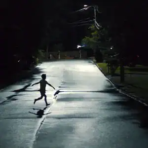 A child runs across a dark suburban street at night in a suspenseful scene from the movie Weapons (2025).