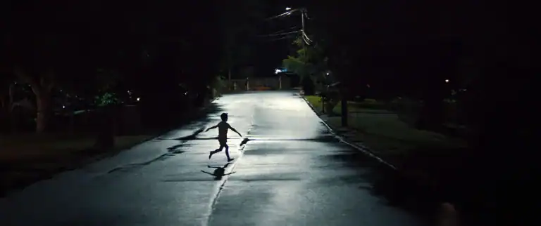 A child runs across a dark suburban street at night in a suspenseful scene from the movie Weapons (2025).